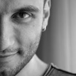 Close-up black and white portrait of a man with a beard smiling.